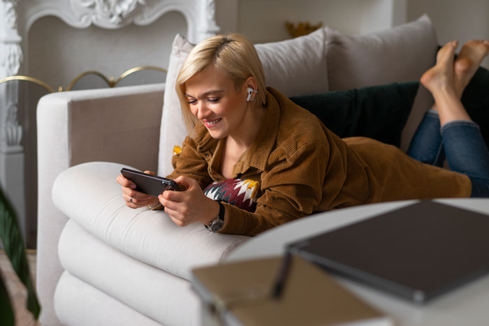 Woman lying on couch smiling at phone, representing stay-at-home mom and teen job discussions at home. Woman lying on couch smiling at phone, representing stay-at-home mom and teen job discussions at home.