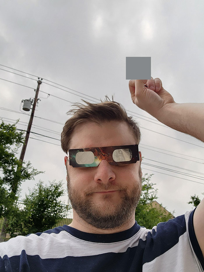 Man wearing eclipse glasses outdoors with cloudy sky, demonstrating nature's power during a solar event.