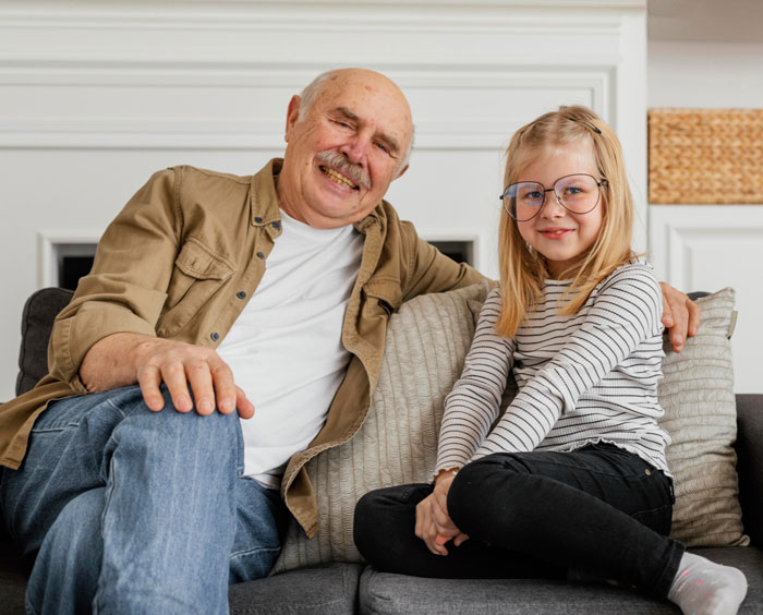 Elderly grandpa sitting with young girl on couch, highlighting years spent taking care of grandpa by family member. Elderly grandpa sitting with young girl on couch, highlighting years spent taking care of grandpa by family member.