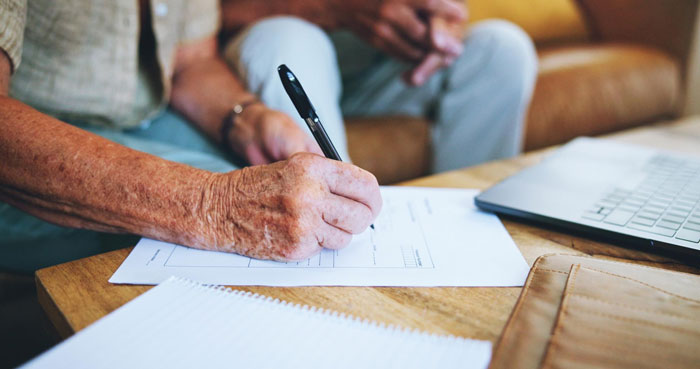Elderly grandpa signing documents at a table with a laptop nearby, symbolizing caregiving and family demands. Elderly grandpa signing documents at a table with a laptop nearby, symbolizing caregiving and family demands.