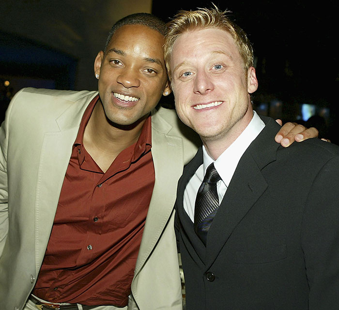 Will Smith's co-actor smiling with a man in a suit, highlighting studio name removal claim in publicity controversy. Will Smith's co-actor smiling with a man in a suit, highlighting studio name removal claim in publicity controversy.