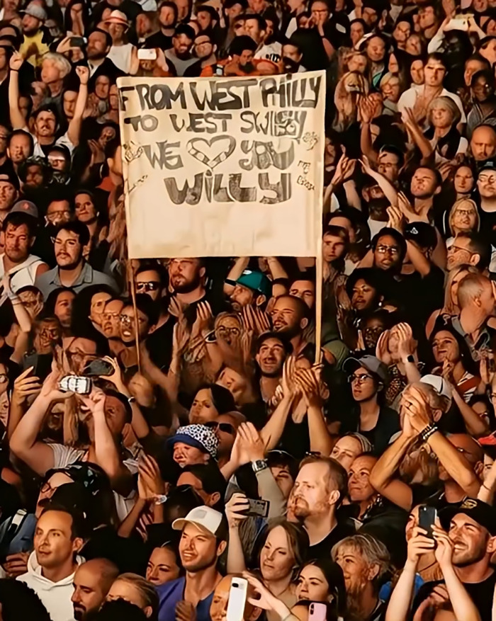 Crowd at event holding sign for Willy with many hands raised in the air, relating to Will Smith faking crowds with AI. Crowd at event holding sign for Willy with many hands raised in the air, relating to Will Smith faking crowds with AI.