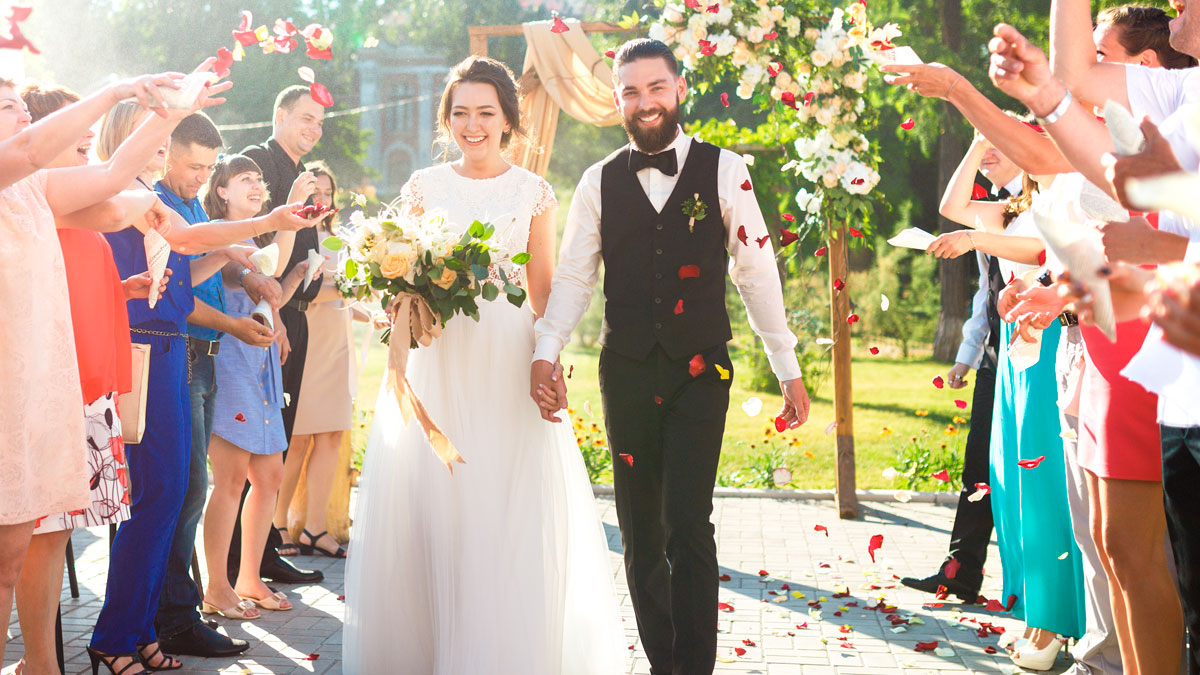 Bride and groom smiling outdoors as guests throw rose petals during a joyful wedding celebration in the same month.