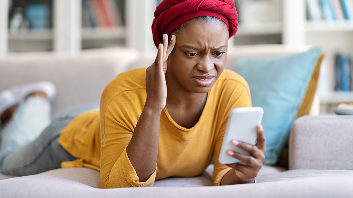 Woman checking boyfriendu2019s phone with a confused and regretful expression while lying on a couch at home