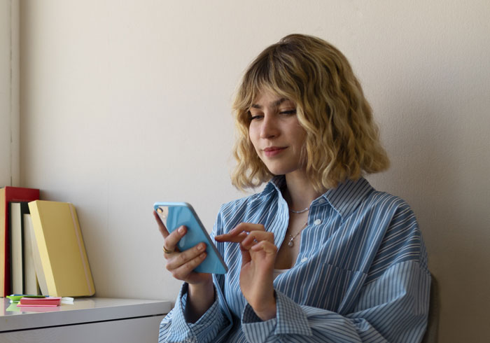 Woman in a striped shirt using a smartphone, representing netizens reacting to AI boyfriend proposal news online. Woman in a striped shirt using a smartphone, representing netizens reacting to AI boyfriend proposal news online.