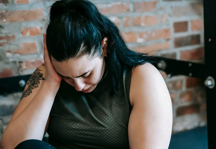 Woman sitting indoors looking down, appearing upset after being told to lose weight by a good friend. Woman sitting indoors looking down, appearing upset after being told to lose weight by a good friend.