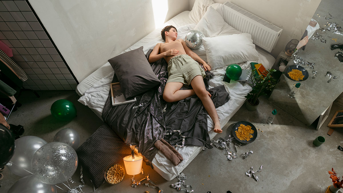Young woman asleep on bed surrounded by party mess, showing consequences of temporary houseguest and missed payments.