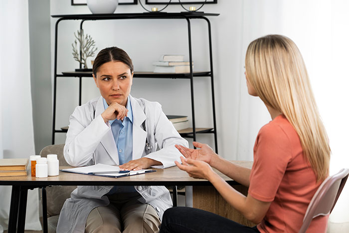 Woman in a medical consultation expressing chronic pain, doctor listening skeptically in a clinical setting. Woman in a medical consultation expressing chronic pain, doctor listening skeptically in a clinical setting.