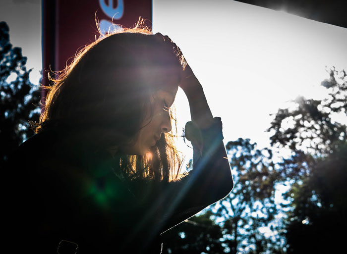Silhouetted woman holding her head outdoors in sunlight, expressing stress related to autistic nephew refusing babysitting. Silhouetted woman holding her head outdoors in sunlight, expressing stress related to autistic nephew refusing babysitting.