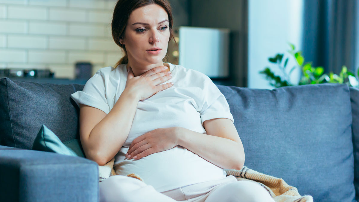 Pregnant woman sitting on couch looking worried and thoughtful, reflecting on family and expectations.