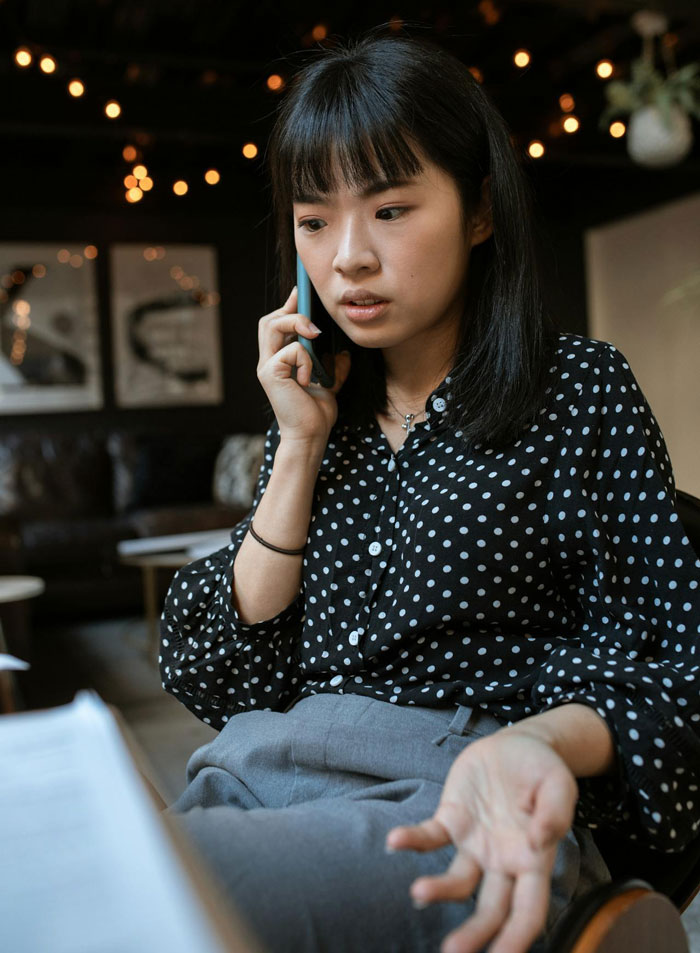 Young woman in polka dot blouse talking on phone, appearing frustrated while discussing babysitters and living wage. Young woman in polka dot blouse talking on phone, appearing frustrated while discussing babysitters and living wage.