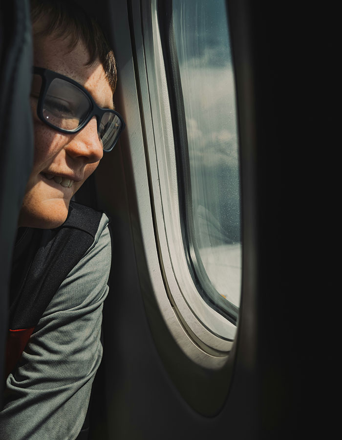 Child looking out airplane window during flight, illustrating passenger experience with bored child sparking debate on flight. Child looking out airplane window during flight, illustrating passenger experience with bored child sparking debate on flight.