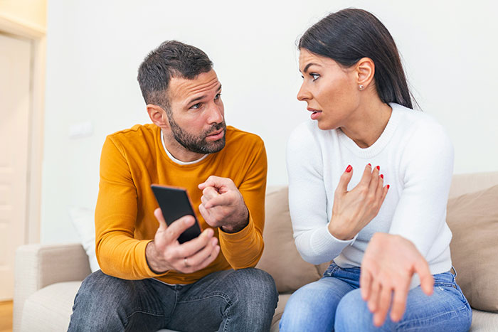 Woman looks frustrated and financially trapped as her jobless fiancé explains himself while holding a phone at home. Woman looks frustrated and financially trapped as her jobless fiancé explains himself while holding a phone at home.