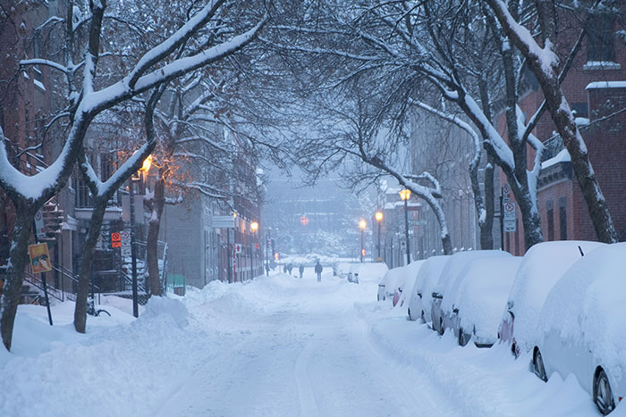 Snow-covered street with parked cars under thick snow, illustrating challenges causing employee misses work due to flat tire.