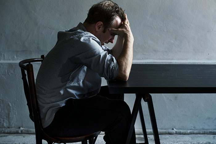 Man sitting at dark table with head in hands, symbolizing man wrongfully jailed and refusing to take down website. Man sitting at dark table with head in hands, symbolizing man wrongfully jailed and refusing to take down website.