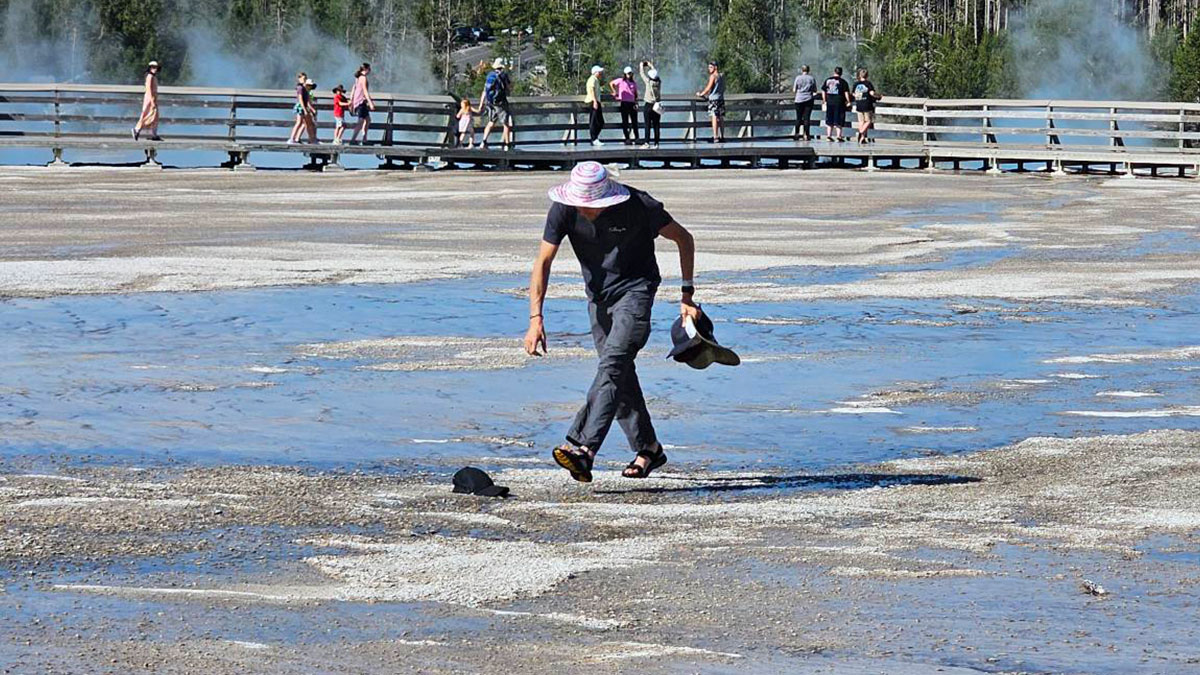 Visitor walking across forbidden area in Yellowstone park while others stay on the designated boardwalk path.