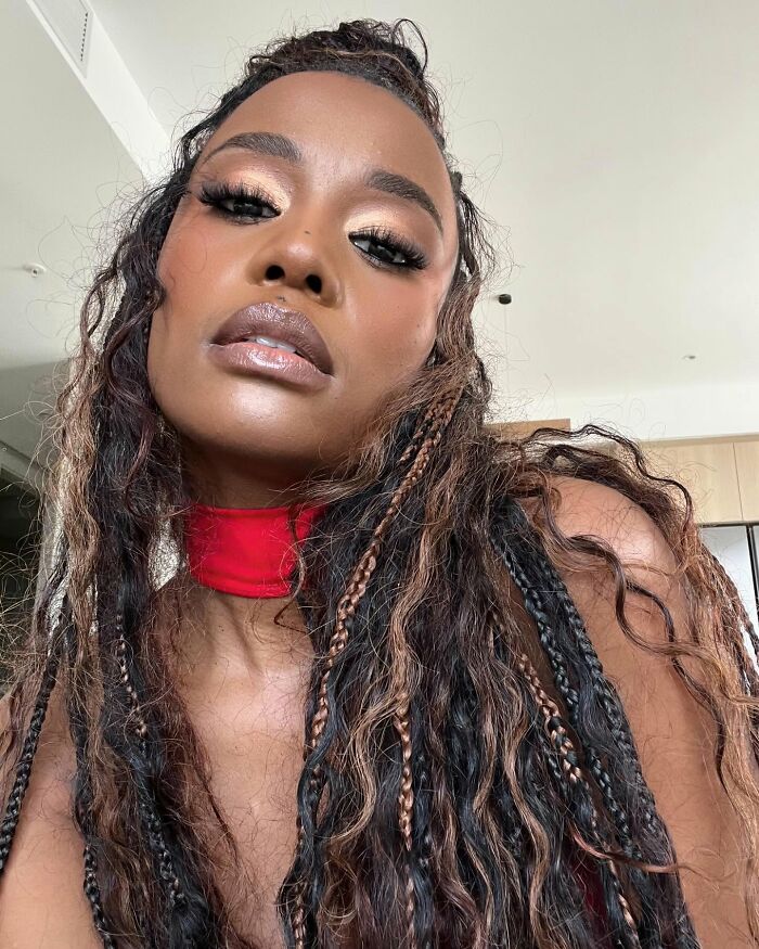 Close-up portrait of a Miss Universe winner with braided hair and glowing makeup in a modern indoor setting.