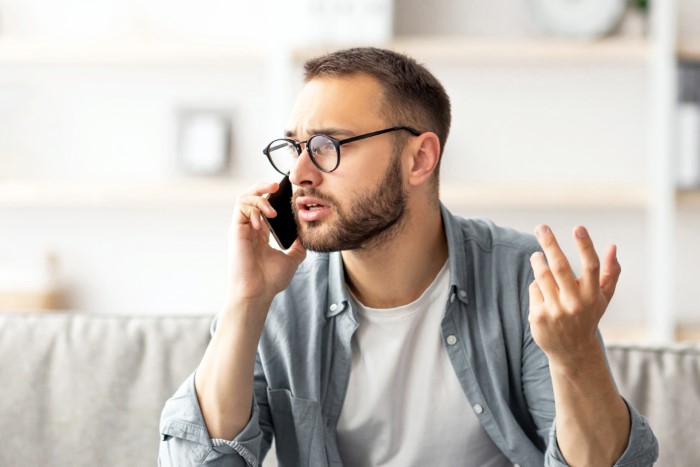 Man wearing glasses looks frustrated while talking on the phone, illustrating babysitting and going MIA situations. Man wearing glasses looks frustrated while talking on the phone, illustrating babysitting and going MIA situations.