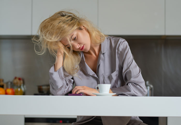 Woman in pajamas looking stressed and tired at kitchen table, reflecting on fears about motherhood challenges.