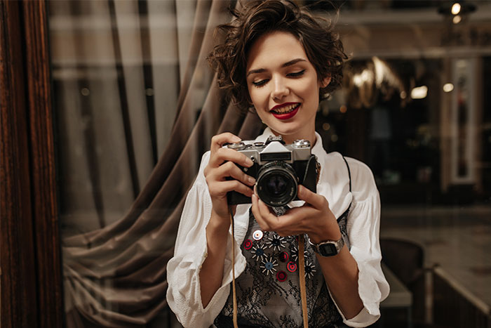Young woman holding a camera, smiling indoors, illustrating man catching a friend stealing his boyfriend’s camera scenario. Young woman holding a camera, smiling indoors, illustrating man catching a friend stealing his boyfriend’s camera scenario.