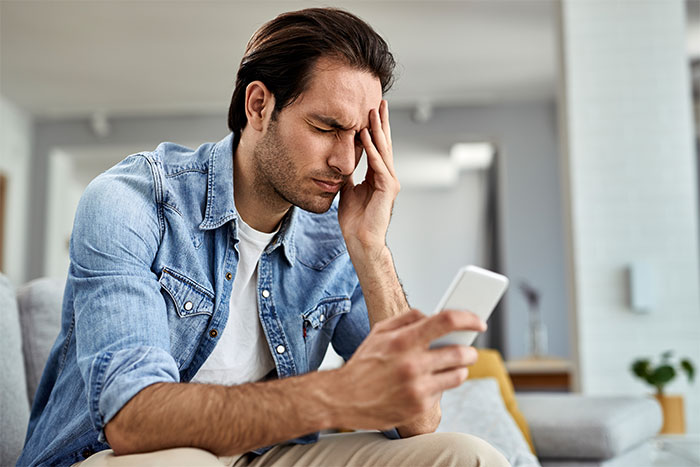 Man in denim jacket looking stressed while holding a smartphone, reflecting on friend stealing boyfriend’s camera. Man in denim jacket looking stressed while holding a smartphone, reflecting on friend stealing boyfriend’s camera.