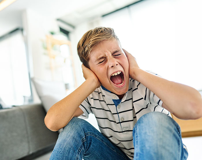 Young boy having a meltdown indoors covering ears upset about mountain biking early in the morning. Young boy having a meltdown indoors covering ears upset about mountain biking early in the morning.