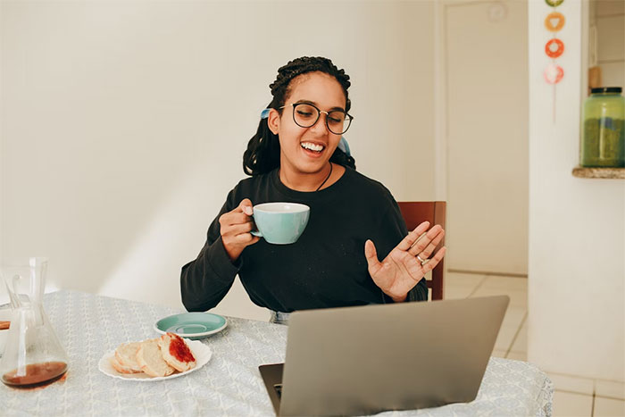 Woman showing up unannounced at doorstep, holding a cup and interacting with a laptop in a casual home setting. Woman showing up unannounced at doorstep, holding a cup and interacting with a laptop in a casual home setting.