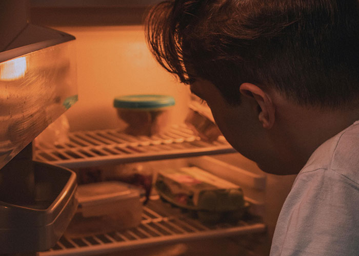 Young man looking inside a fridge filled with leftovers, related to roommate stealing and habanero cake prank.