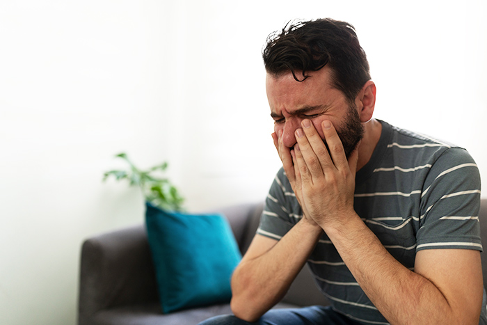 Man covering face with hands, showing distress while sitting on a couch during a widow and single mom date story. Man covering face with hands, showing distress while sitting on a couch during a widow and single mom date story.