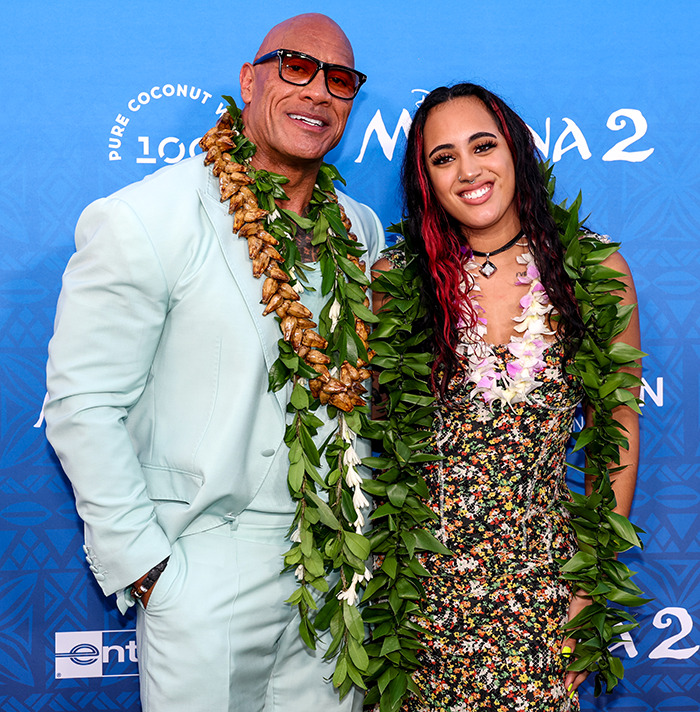 The Rock's daughter smiling with The Rock, both wearing leis at a movie premiere event. The Rock's daughter smiling with The Rock, both wearing leis at a movie premiere event.