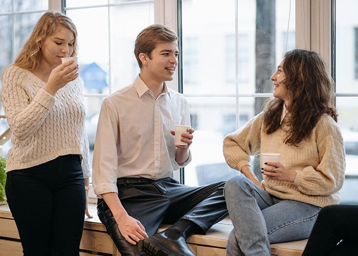 Three young adults having coffee indoors, with the guy clearly not into the conversation, showing uneasy body language.