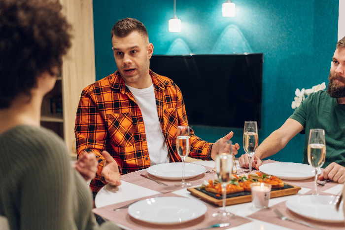 Man in orange plaid shirt joking at dinner table with twin brother and woman about trading wife for younger woman. Man in orange plaid shirt joking at dinner table with twin brother and woman about trading wife for younger woman.