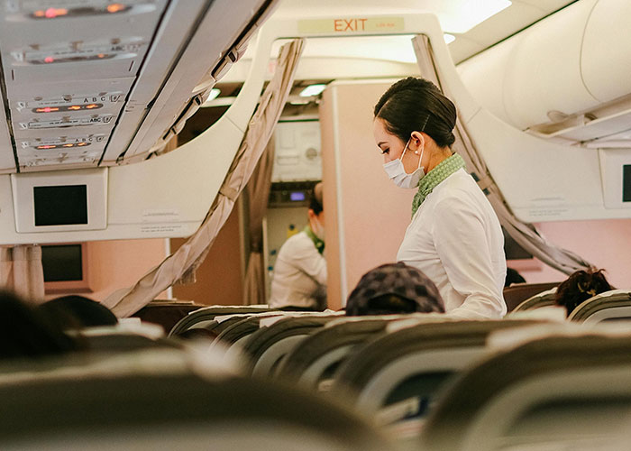 Flight attendant wearing a mask assisting passengers inside an airplane cabin during a commercial flight. Flight attendant wearing a mask assisting passengers inside an airplane cabin during a commercial flight.