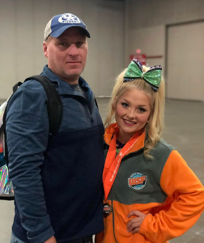 Man wearing a cap stands next to a smiling cheerleader with a large bow, highlighting cheerleader university news story. Man wearing a cap stands next to a smiling cheerleader with a large bow, highlighting cheerleader university news story.