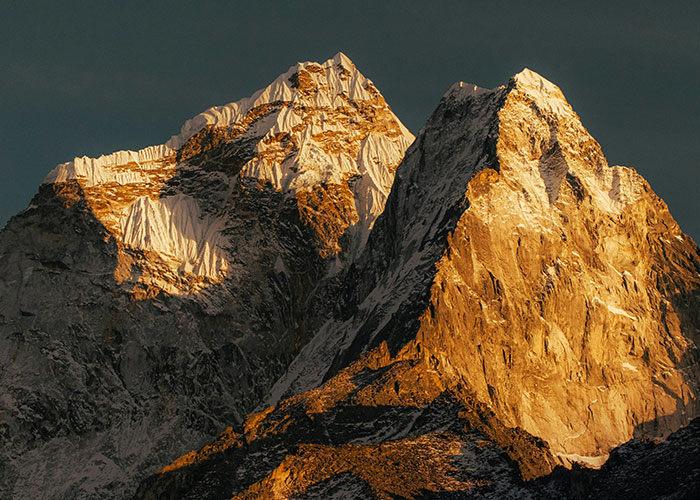 Sunlit towering mountain peaks under a dark sky, evoking a sense of terrifying true stories and awe-inspiring nature.