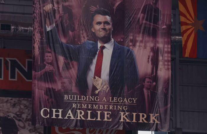 Banner displaying Charlie Kirk in a suit and tie with fist raised, related to WWE level stuff and memorial event controversy. Banner displaying Charlie Kirk in a suit and tie with fist raised, related to WWE level stuff and memorial event controversy.