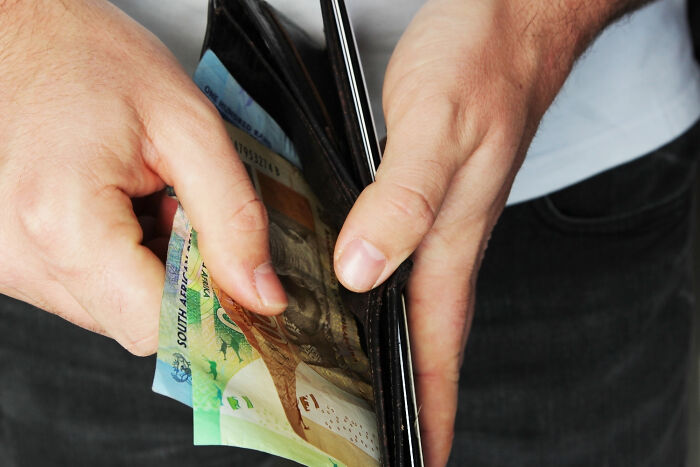 Person holding a wallet with South African banknotes, illustrating a mind-boggling conversation about adult finances.
