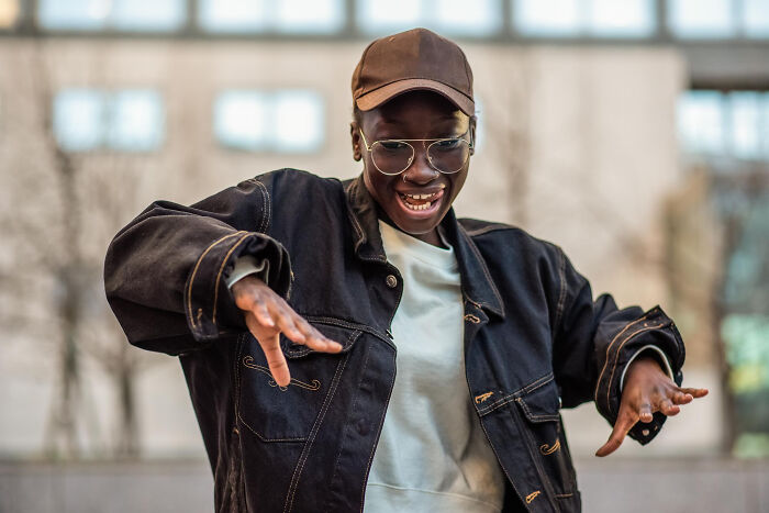 Person wearing glasses and a cap smiling joyfully, illustrating childish reasons ladies ditched a guy in casual urban setting.