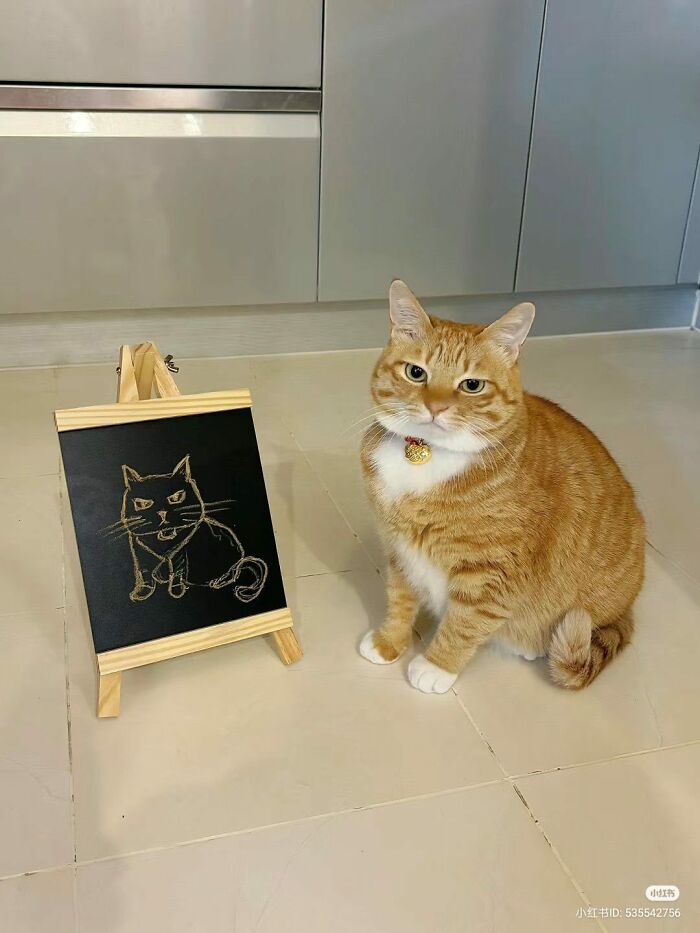Adorable ginger cat sitting beside a small easel with a cat drawing, showcasing top-tier work and charm.