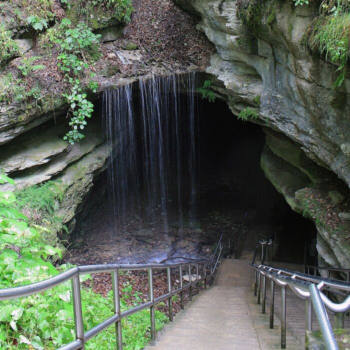 Entrance to a dark cave beneath a waterfall with stairs leading down, exploring terrifying true stories underground.