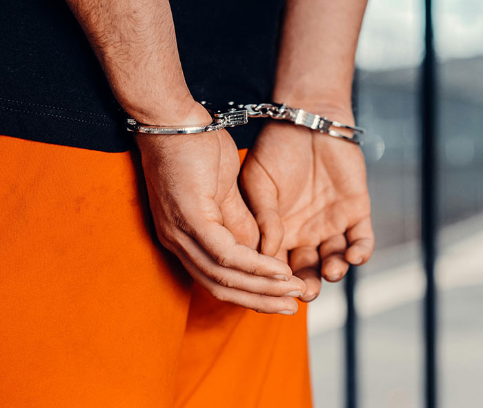 Close-up of a person in handcuffs wearing an orange uniform, symbolizing a teacher arrested at school for causing damage and sickness. Close-up of a person in handcuffs wearing an orange uniform, symbolizing a teacher arrested at school for causing damage and sickness.