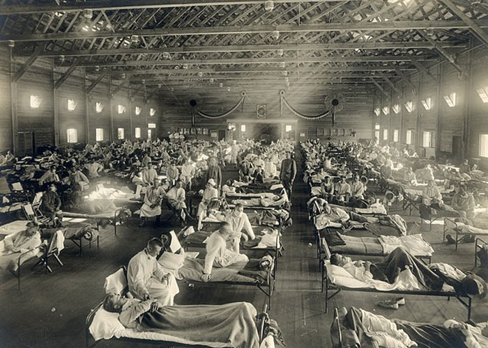 Large historical hospital ward filled with patients and nurses, illustrating damage to society from major events.
