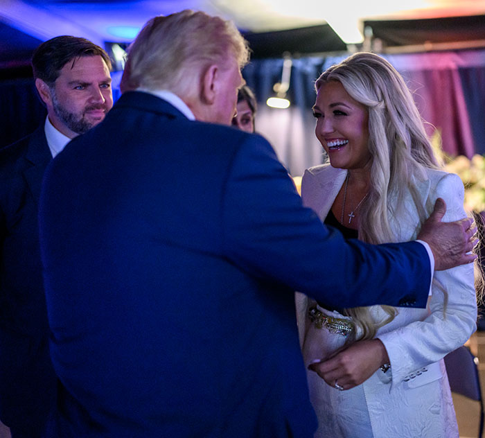 A man in a blue suit engaging with a smiling woman in a white blazer at a WWE level event setting. A man in a blue suit engaging with a smiling woman in a white blazer at a WWE level event setting.