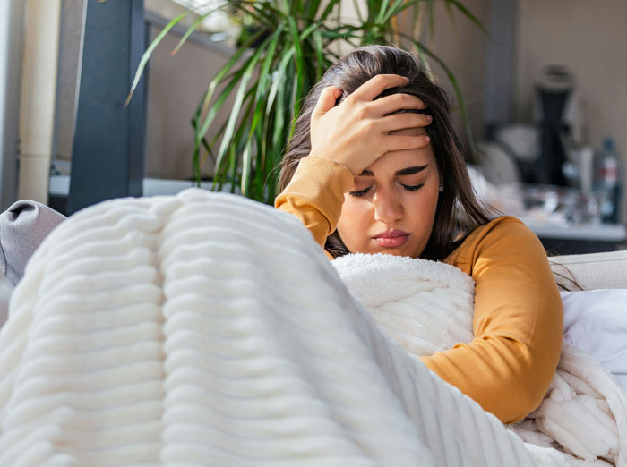 Young woman looking distressed on a couch, reflecting the feeling of getting the ick after a glance at a phone.