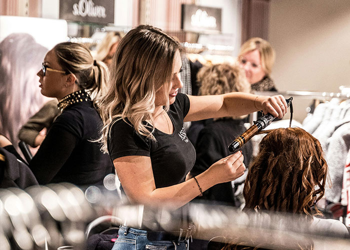 Woman styling hair with curling iron in a busy salon, illustrating common purchases people have ditched due to high price tags
