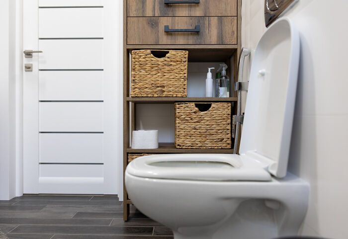 Modern bathroom interior with white toilet and wooden storage shelves featuring woven baskets and toiletries.