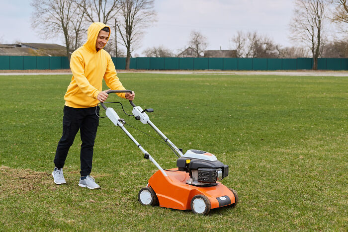 Young man in a yellow hoodie mowing a lawn outdoors, illustrating one of the most childish reasons ladies ditched a guy.