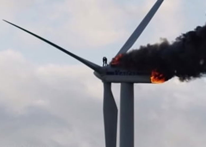 Person standing on burning wind turbine with thick black smoke, illustrating terrifying true stories that are hard to believe.