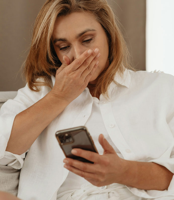 Woman looking shocked at phone, covering mouth with hand, showing reaction to a glance at a phone changing everything.