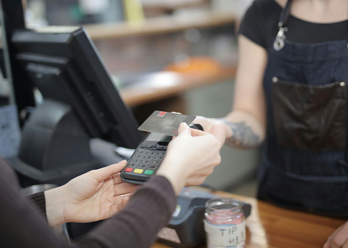 Customer using a credit card to pay at a store counter, highlighting common purchases ditched due to high price tags.